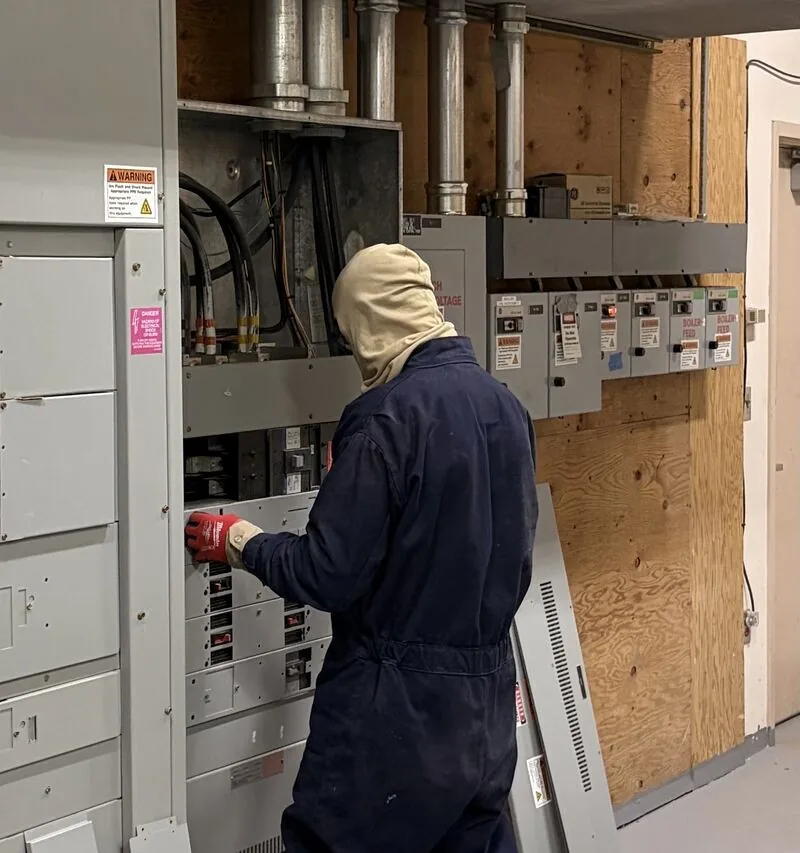 New Phase technician in arc-flash PPE servicing a live panelboard at an Arizona critical facility