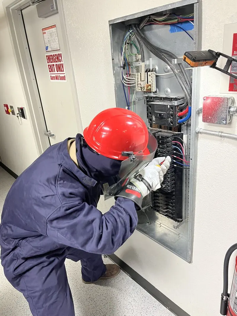 New Phase technician in arc-flash PPE servicing a panel during a preventive maintenance visit, Arizona